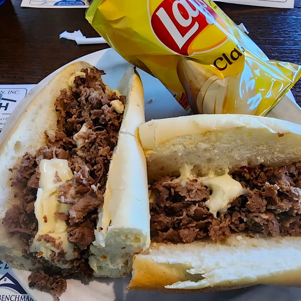 A Green Street Grill cheesesteak sandwich cut in half with a bag of Lay's potato chips.