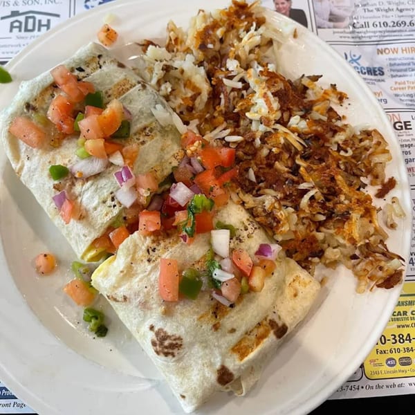 A breakfast burrito topped with pico de gallo, served with a side of crispy hash browns.