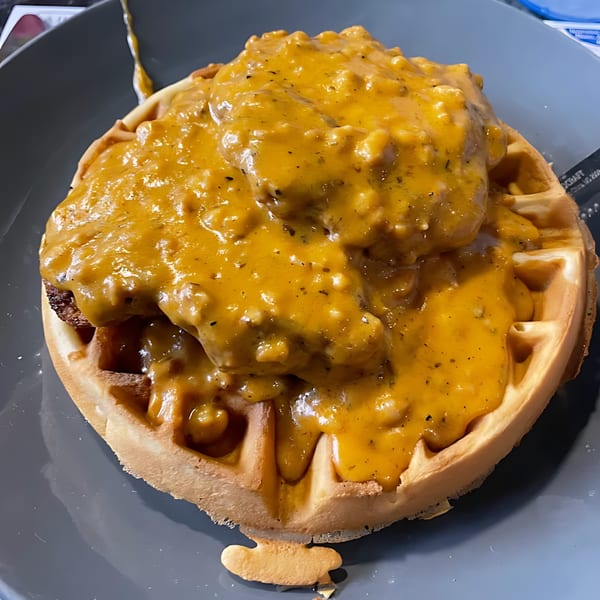 Chicken and waffles from Green Street Grill, smothered in a rich, savory gravy on a gray plate.