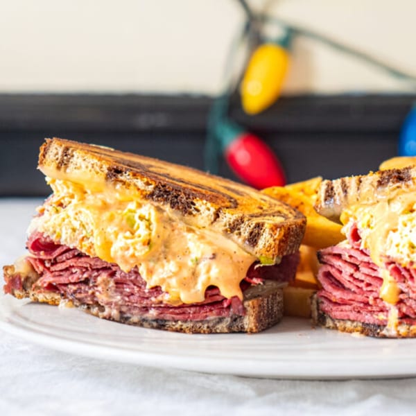 A Green Street Grill Reuben sandwich, cut in half, with fries and colorful lights in the background.