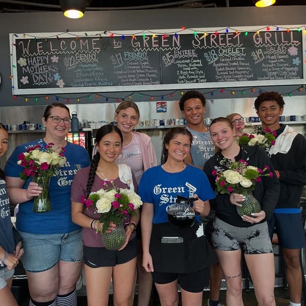 Green Street Grill staff, holding flower bouquets, pose in front of a chalkboard menu.
