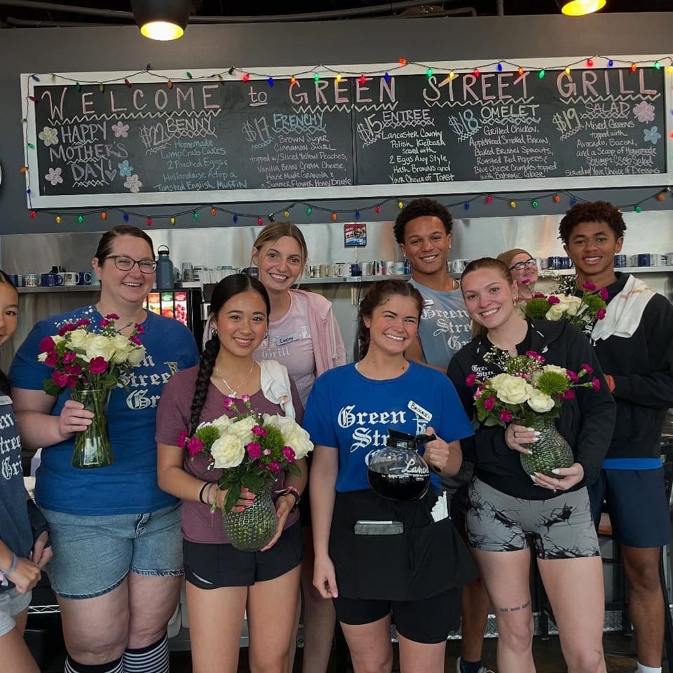 Green Street Grill staff, holding flower bouquets, pose in front of a chalkboard menu.
