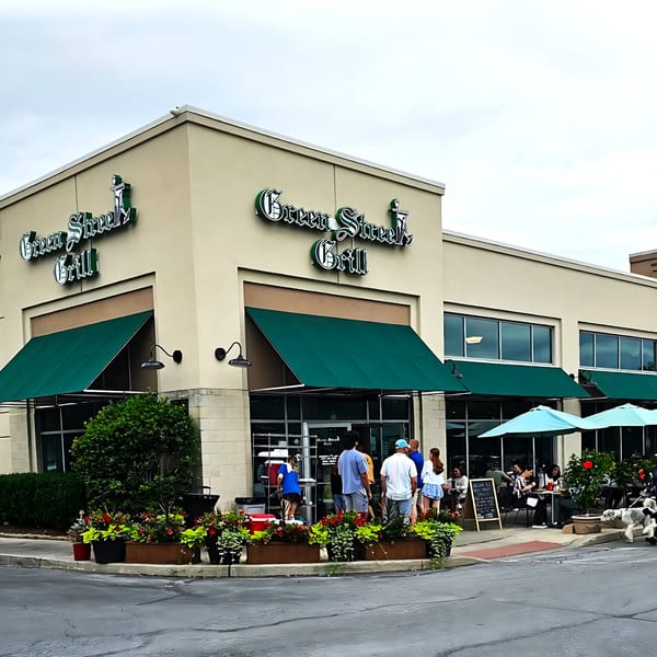 Exterior of Green Street Grill diner with green awnings, outdoor seating, and people waiting outside.