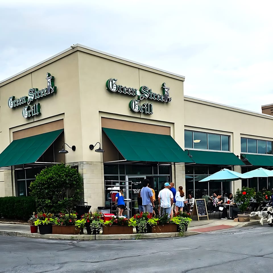 Exterior of Green Street Grill diner with green awnings, outdoor seating, and people waiting outside.