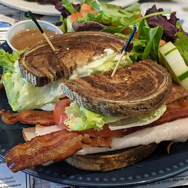 A Green Street Grill club sandwich with bacon, turkey, lettuce, and tomato, served with a side salad.