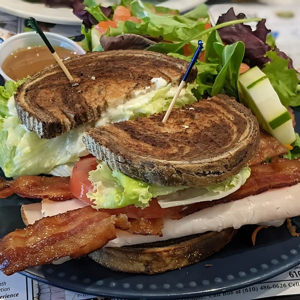 A Green Street Grill turkey club sandwich with bacon, lettuce, and tomato, served with a side salad.