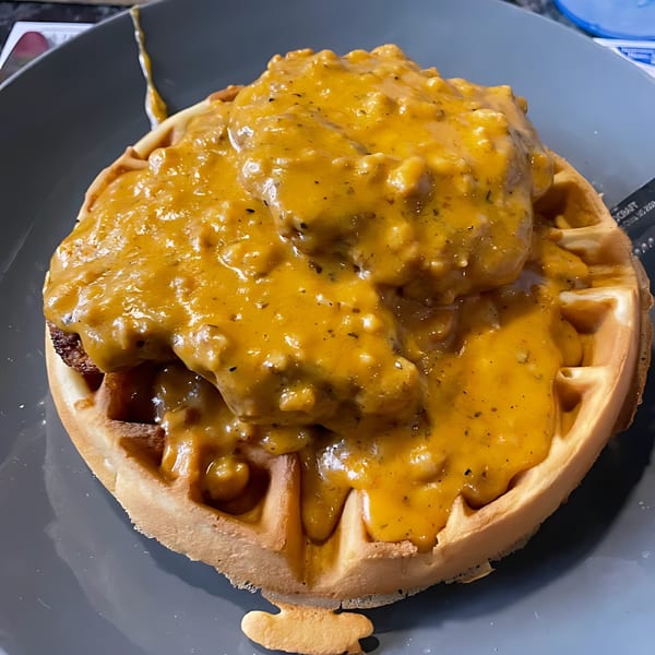 Chicken and waffles from Green Street Grill, smothered in a rich, savory gravy on a gray plate.