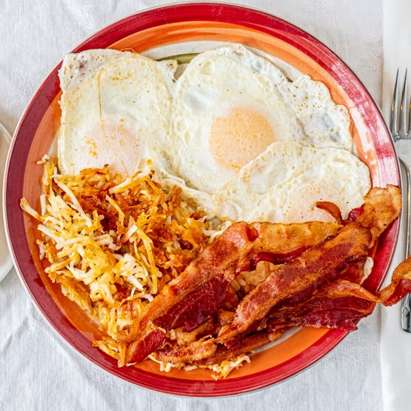A diner breakfast plate with three fried eggs, crispy hash browns, and several strips of bacon.